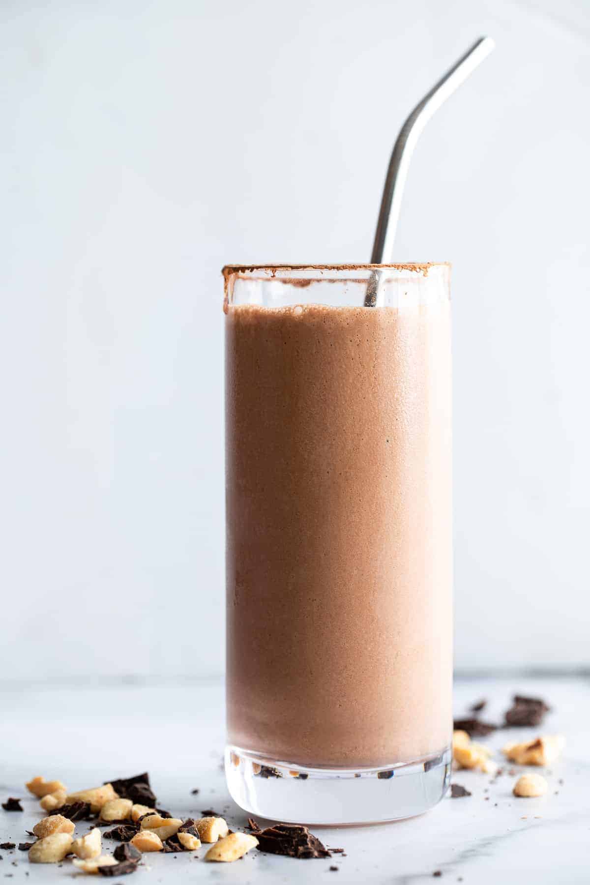 peanut butter chocolate protein shake on a table with peanuts around it