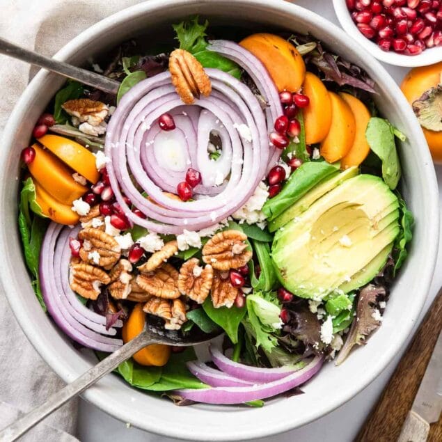 pomegranate persimmon salad in a ceramic bowl with salad tongs